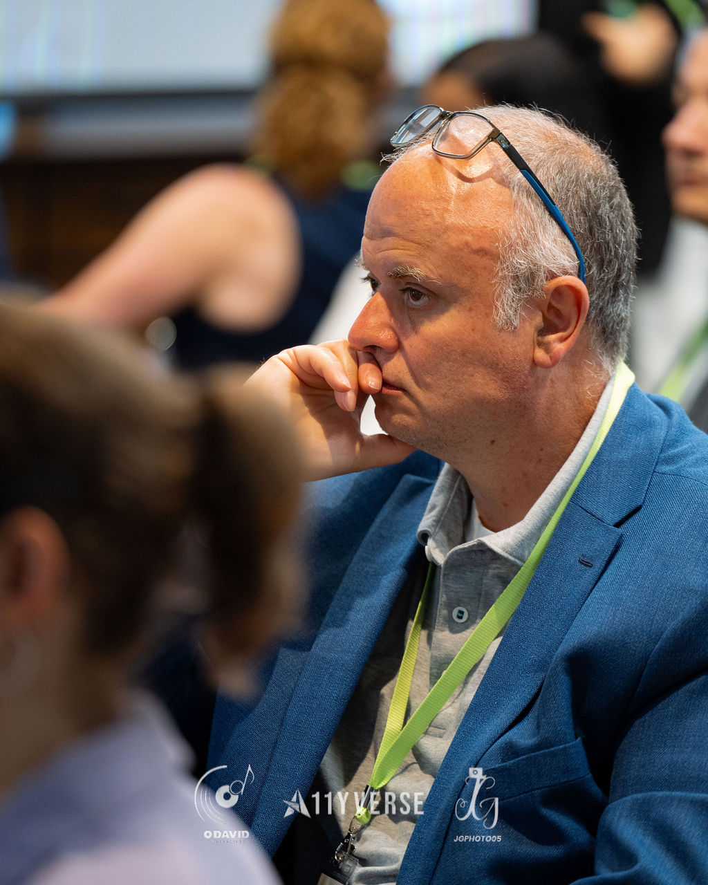 Close portrait of an attendee with glasses pushed up on the forehead, resting a hand near the face while listening thoughtfully.
