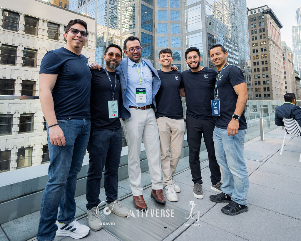 Six people pose together and smile on an outdoor rooftop terrace, with city office towers rising behind them.